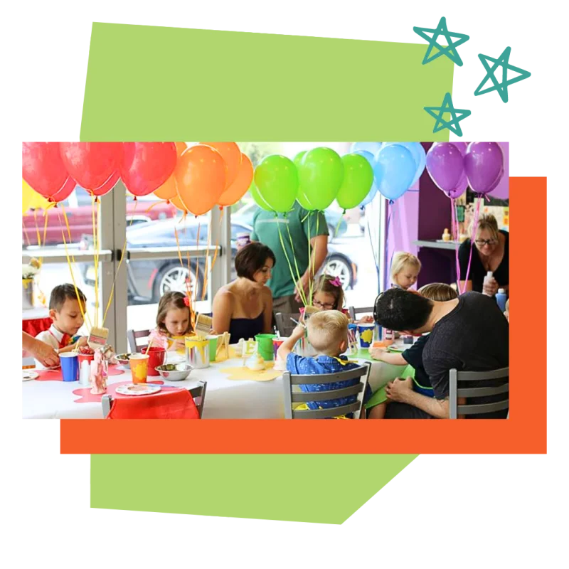 A woman surrounded by children sitting around her at a Color Café studio, enjoying a creative pottery painting activity.