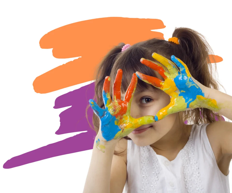 A girl with paint on her hands making a triangle shape in front of her eye during a creative painting session at Color Café.